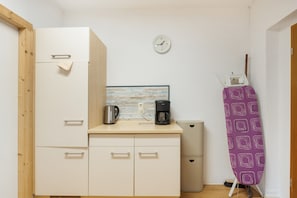 A compact kitchenette with a coffee maker, a kettle, and a clock on the wall.