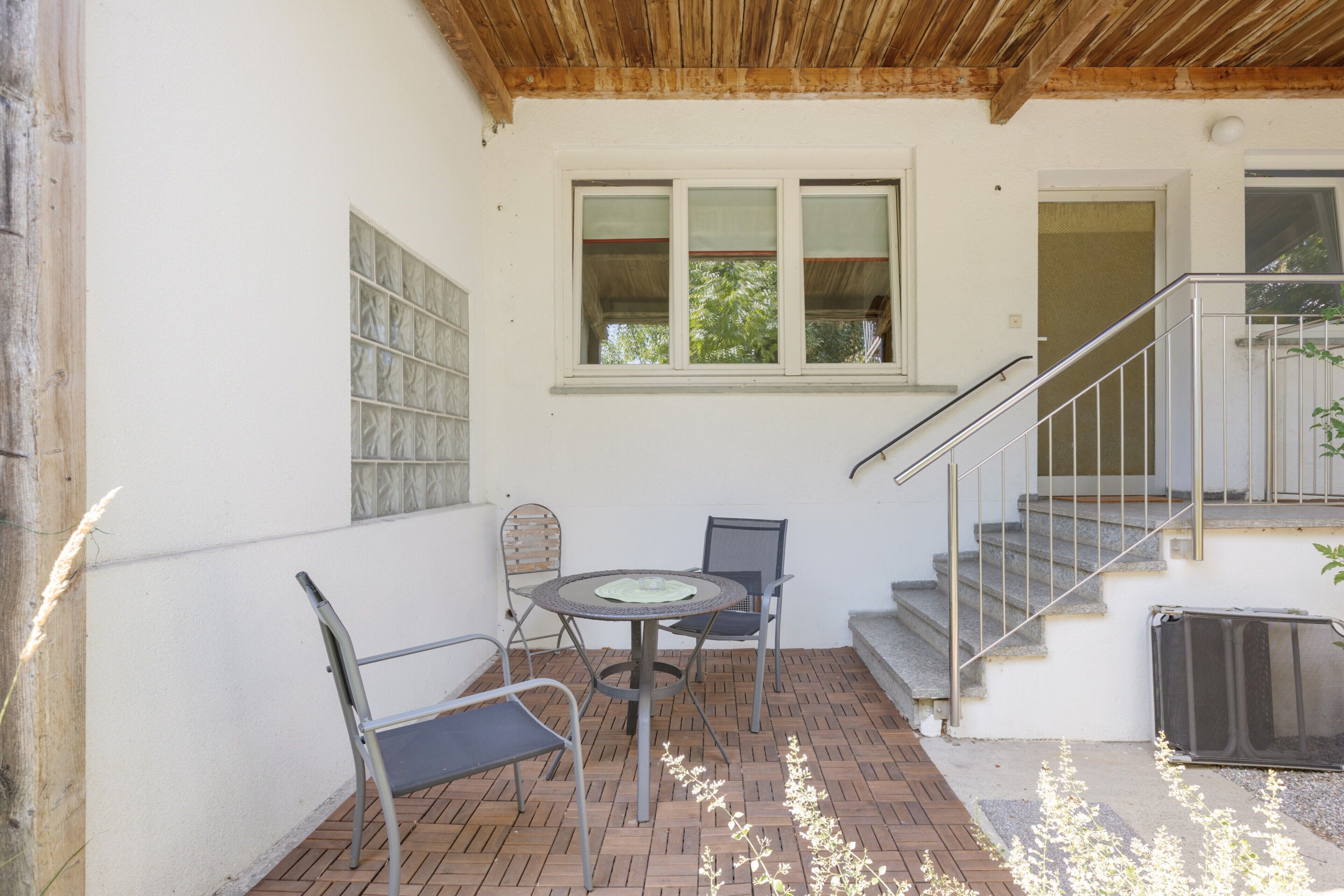 A patio with a table and chairs, a window with blinds, and a staircase.