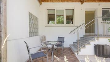 A patio with a table and chairs, a window with blinds, and a staircase.