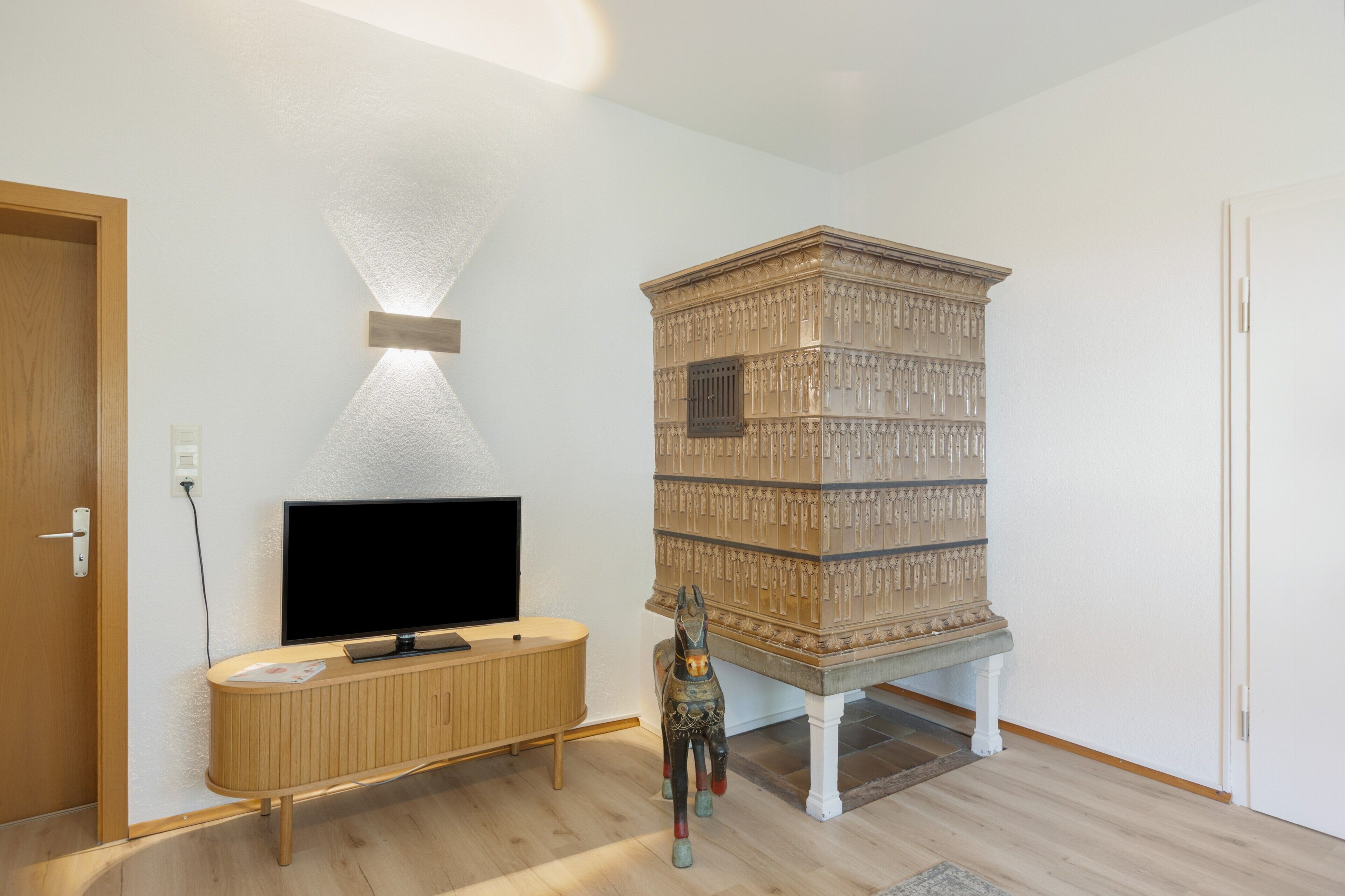 A room with a wooden TV stand, a flat-screen TV, a decorative cabinet, and a small statue.