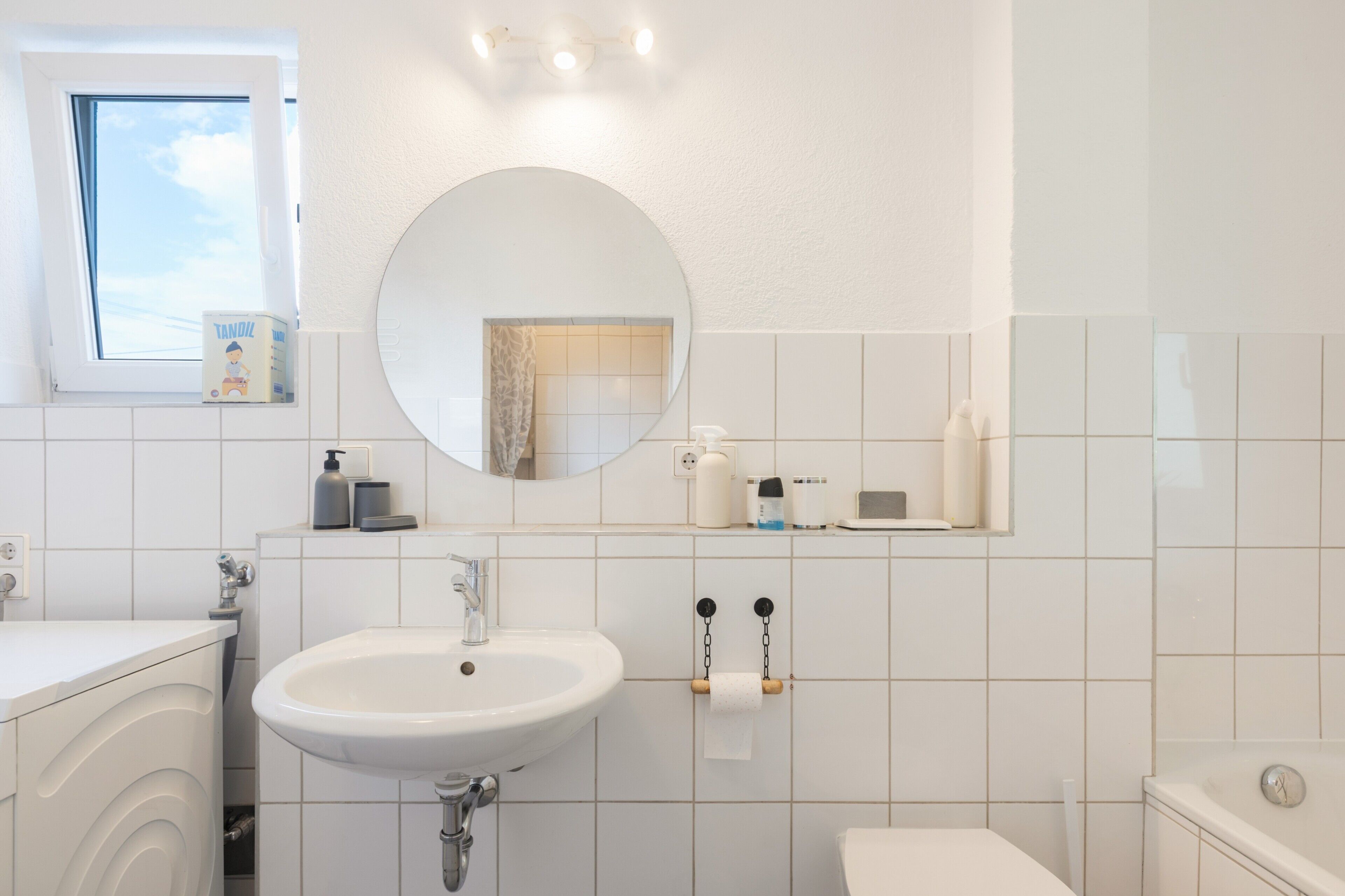 Ein Badezimmer mit einem weißen Waschbecken, einem Spiegel und einem Fenster.