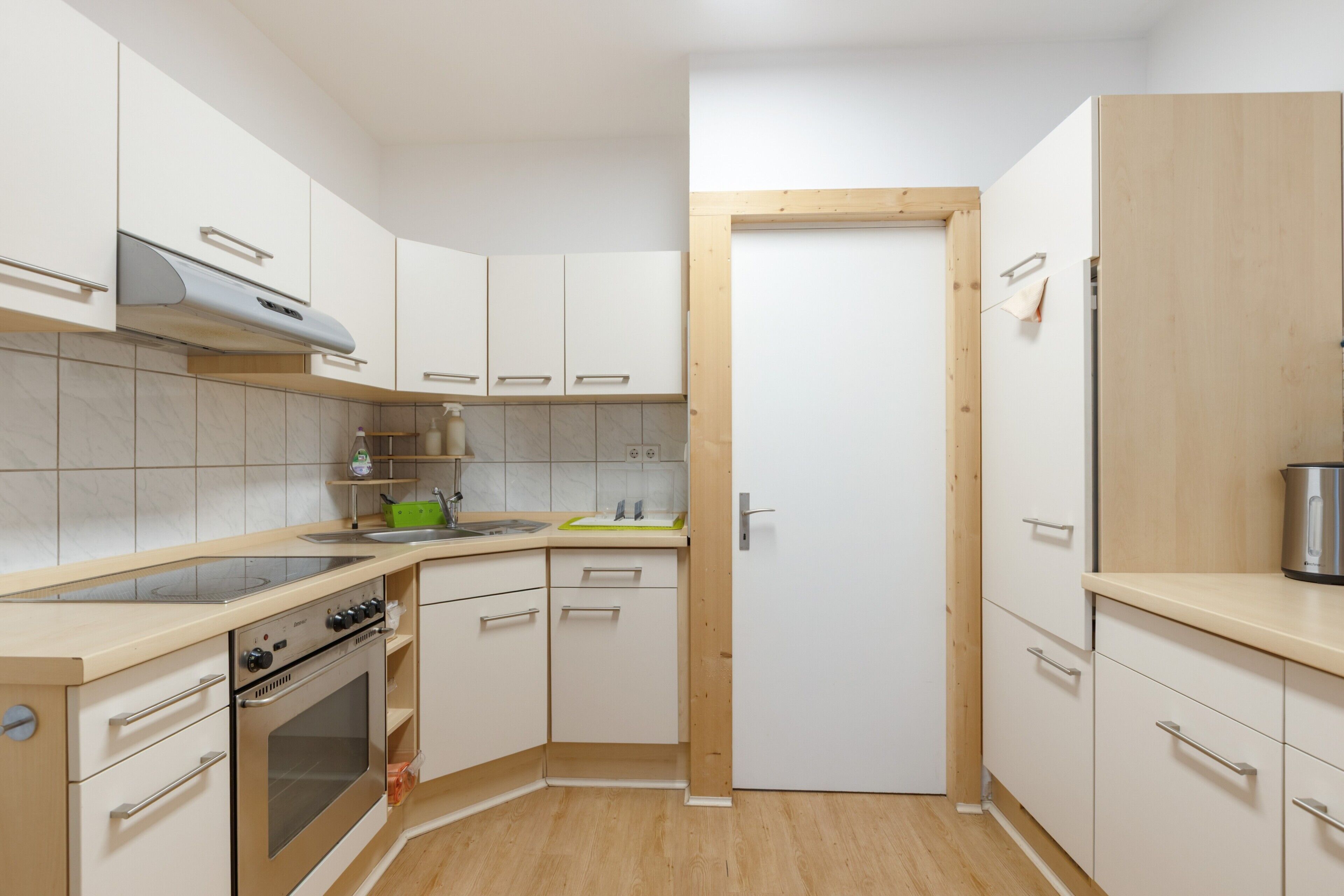 A compact kitchen with white cabinets, a stainless steel oven, and a wooden door.