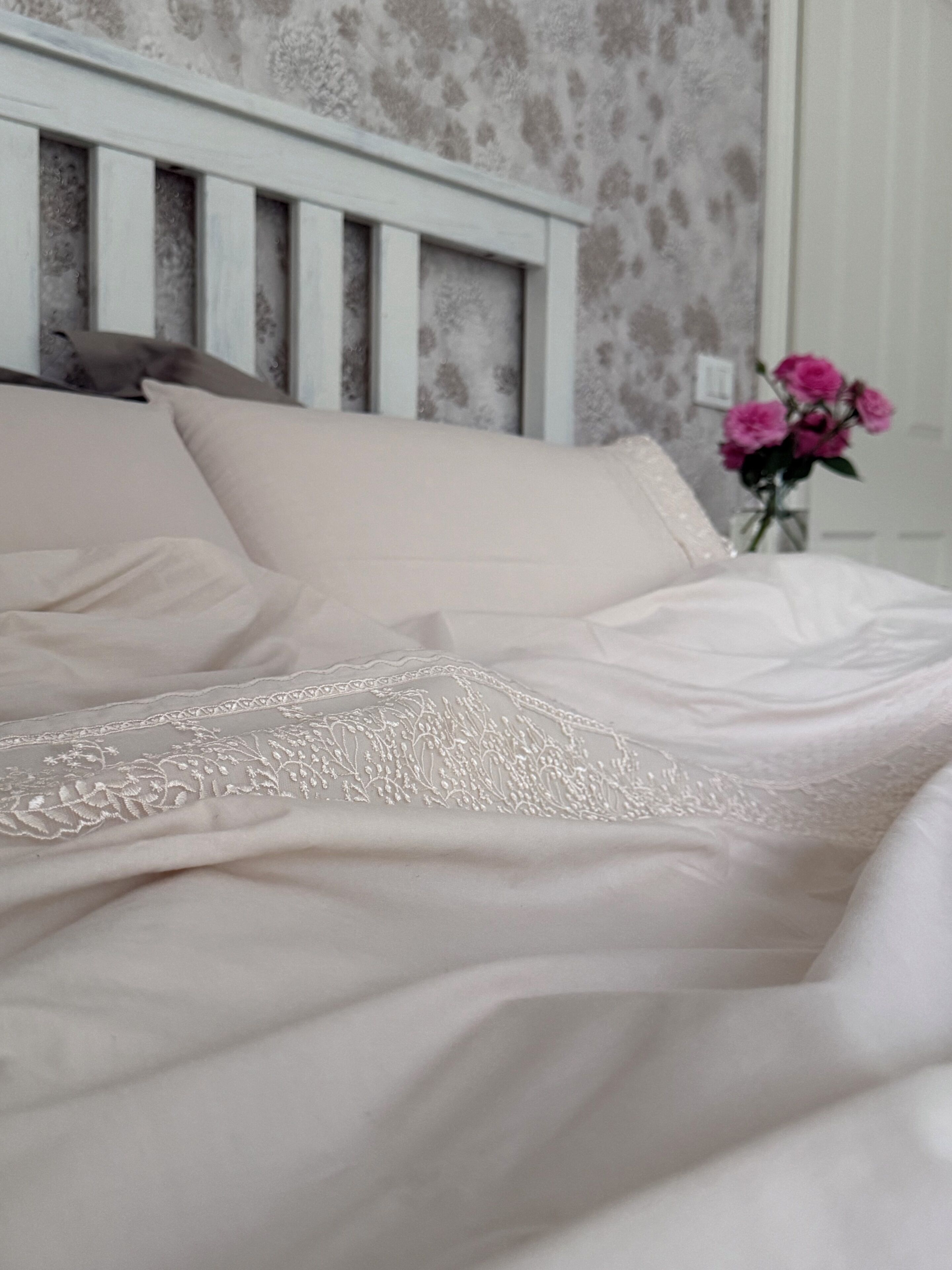 Ein Bett mit weißem Kopfteil und einer Wand mit Blumenmuster.