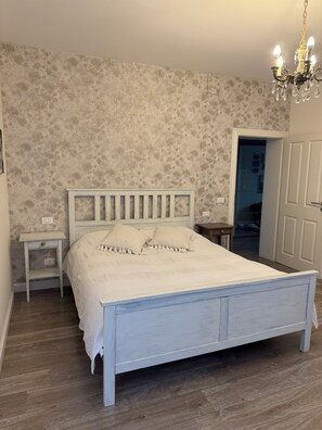 A bedroom with a bed, a nightstand, a dresser, a chandelier, and a door leading to another room. - Panoramic villa in the Euganean Hills, between Bosco, Terme, and Venice (E. Fermi)