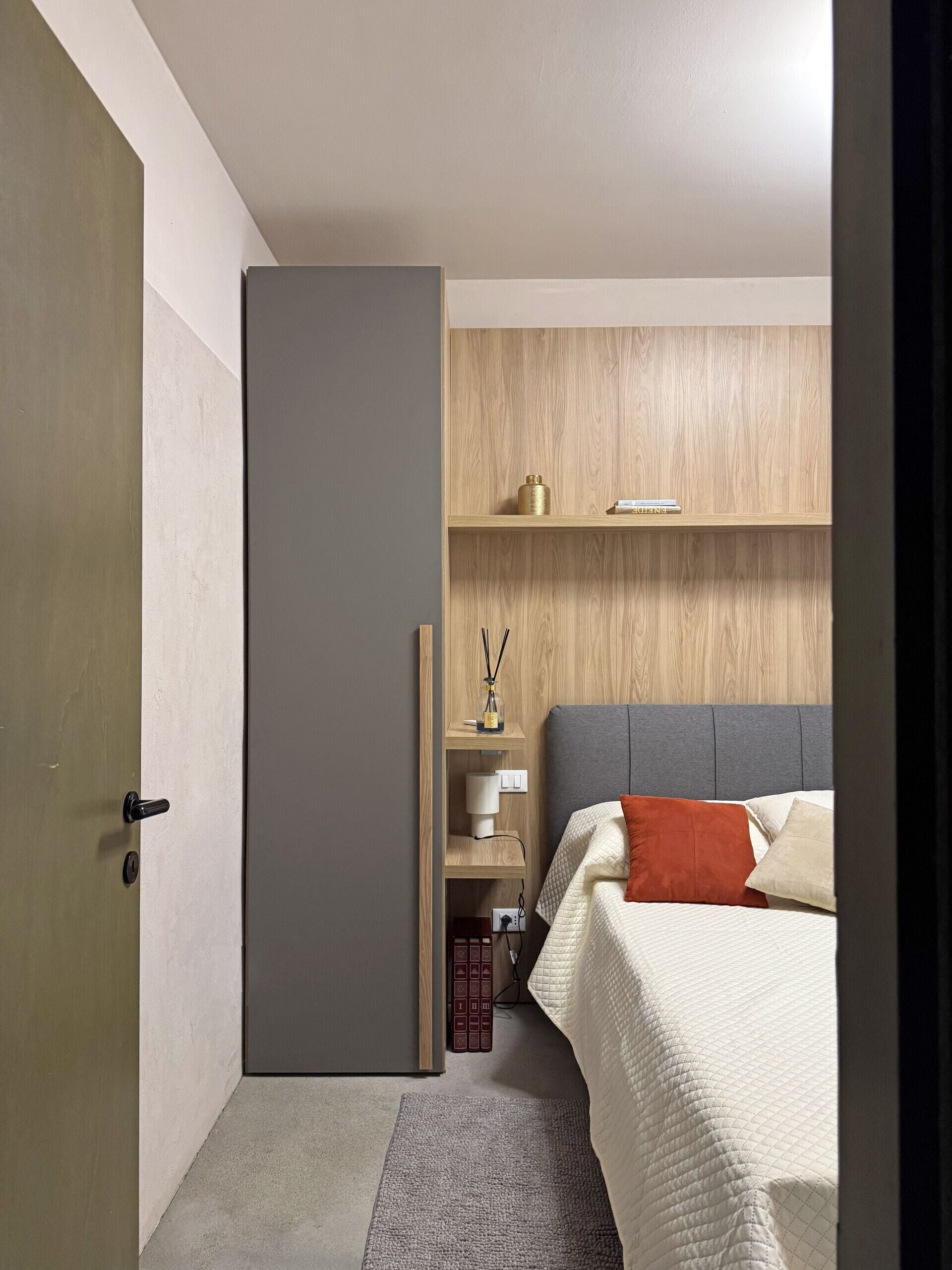 Ein Schlafzimmer mit einem Bett, einem Nachttisch, einem Holzregal und einer Tür.
