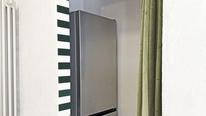 Un angolo di stanza con un frigorifero in acciaio inox, un termosifone e una parete a righe.