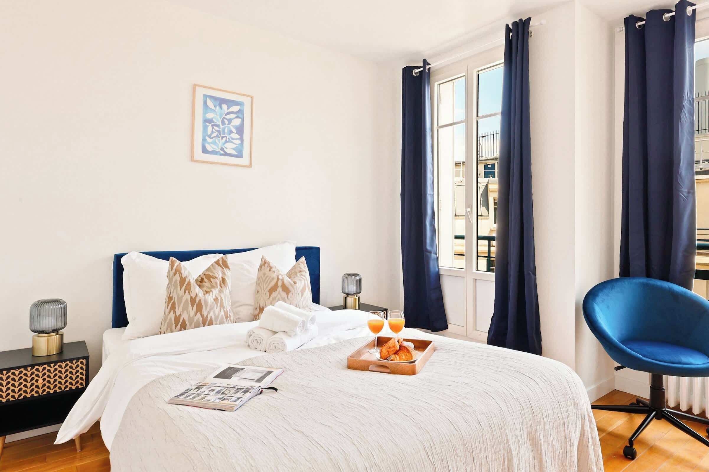 A neatly made bed with a white comforter, two pillows, and a tray with croissants and orange juice.