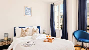 A neatly made bed with a white comforter, two pillows, and a tray with croissants and orange juice.