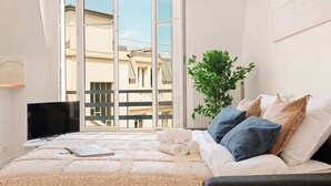A bedroom with a bed, a plant, and a view of buildings through a glass door.