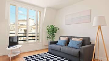 A living room with a grey sofa, a black and white patterned rug, a television on a white table, and a floor lamp.