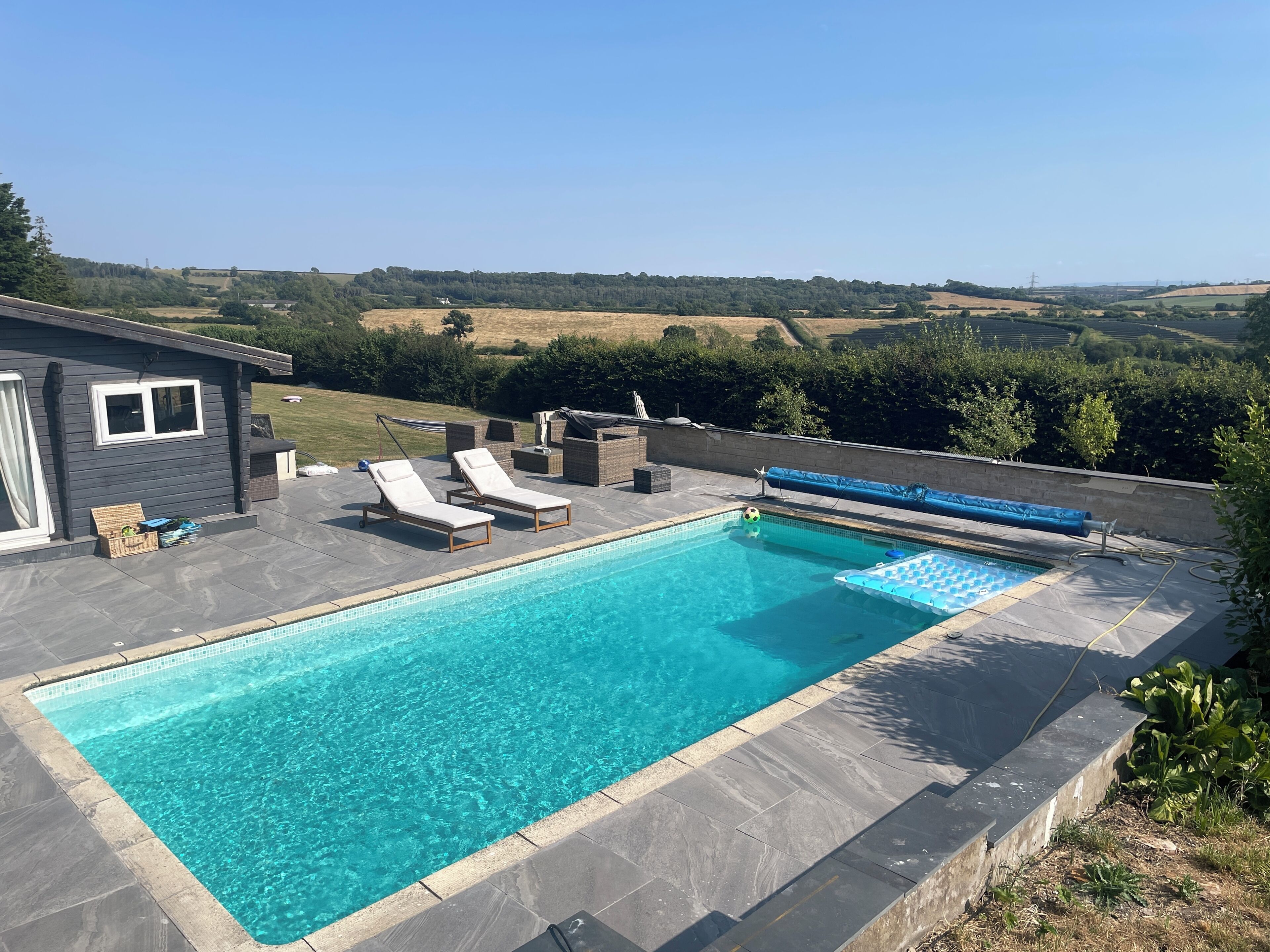 A rectangular swimming pool with two lounge chairs and a small deck area.
