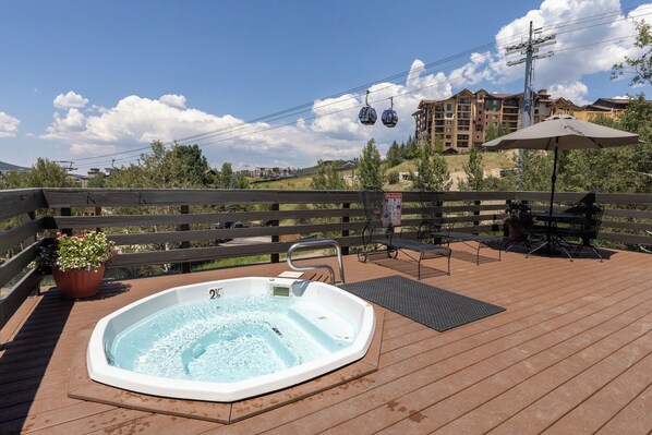 Ein Whirlpool auf einer Holzterrasse mit Blick auf ein Gebäude und eine Seilbahn im Hintergrund.