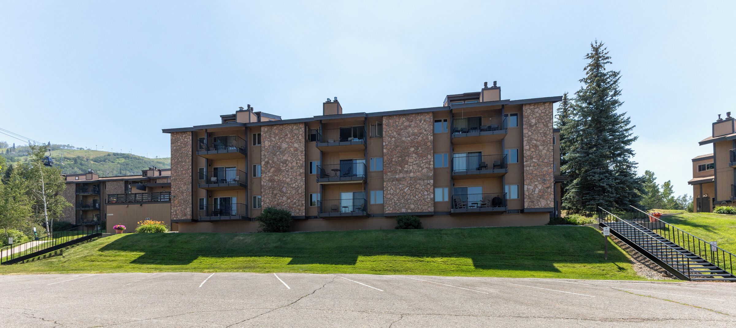 A multi-story residential building with balconies, a parking lot, and a grassy area in front.