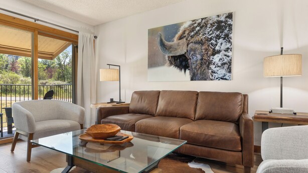 Un salon moderne avec une table basse en verre, un canapé en cuir et un grand tableau représentant un paysage enneigé.