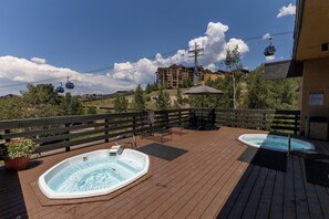 A wooden deck with two hot tubs, a table with chairs, and a sign indicating spa rules. - Ski In/Out | A/C in Summer | Fresh Renovation 2026 (Steamboat Springs)