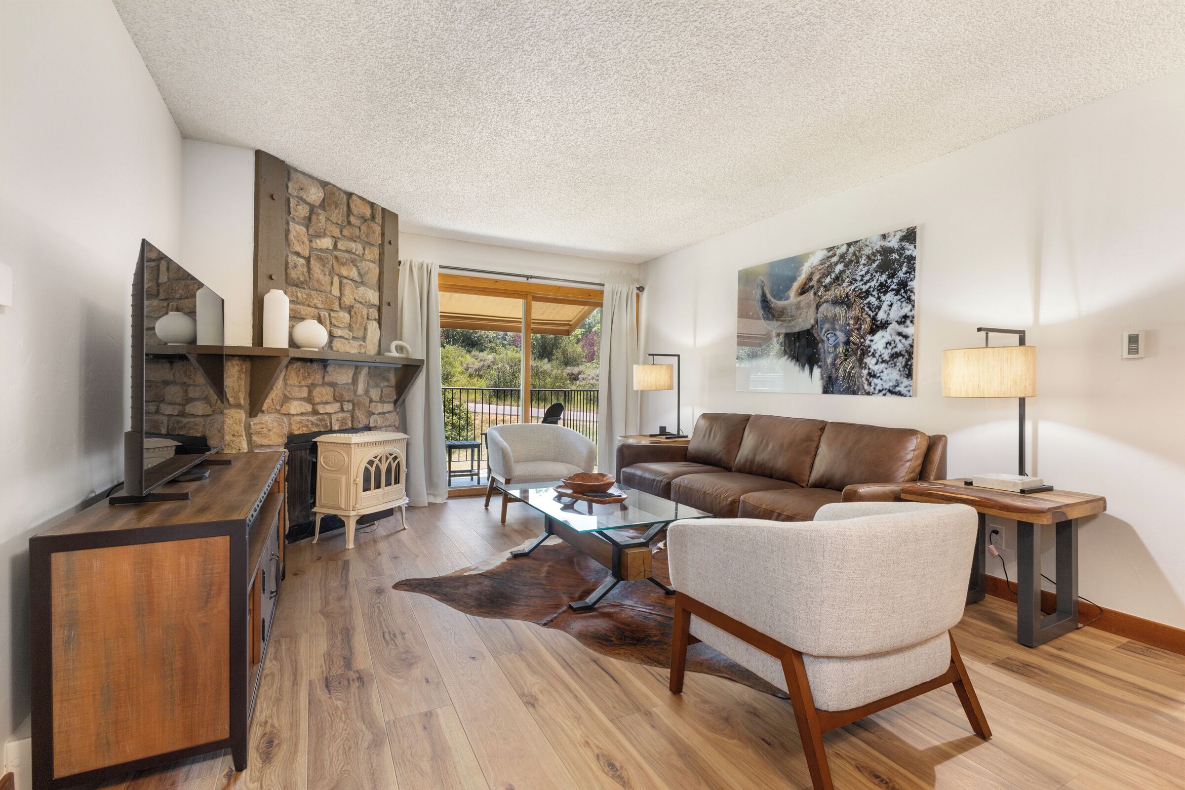 A modern living room with a stone fireplace, leather sofa, and a glass coffee table.