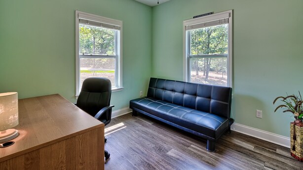 A room with a desk, a black leather sofa, two windows, and a ceiling fan. - 3-bedroom 2-bathroom house centrally located Camden side of Lake Wateree! (Camden)