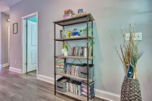Ein Flur mit Bücherregal, gefüllt mit Büchern und DVDs, einer dekorativen Vase mit Zweigen und einer Tür zu einem anderen Raum.