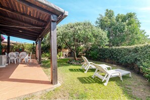 An outdoor patio with a wooden pergola, a stone wall, and a seating area with plastic chairs. - Villetta Alberto: Apartment with Private Terrace, Garden, and Air Conditioning (Palau)