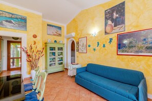A room with a blue sofa, a green cabinet, and a wall decorated with various items including a map and seahorse decorations. - Villetta Alberto: Apartment with Private Terrace, Garden, and Air Conditioning (Palau)