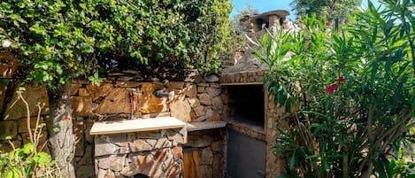 A stone-built outdoor kitchen area with a built-in grill and a stone bench.