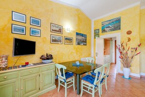 A dining area with a glass table, chairs, and a TV on the wall. - Villetta Alberto: Apartment with Private Terrace, Garden, and Air Conditioning (Palau)