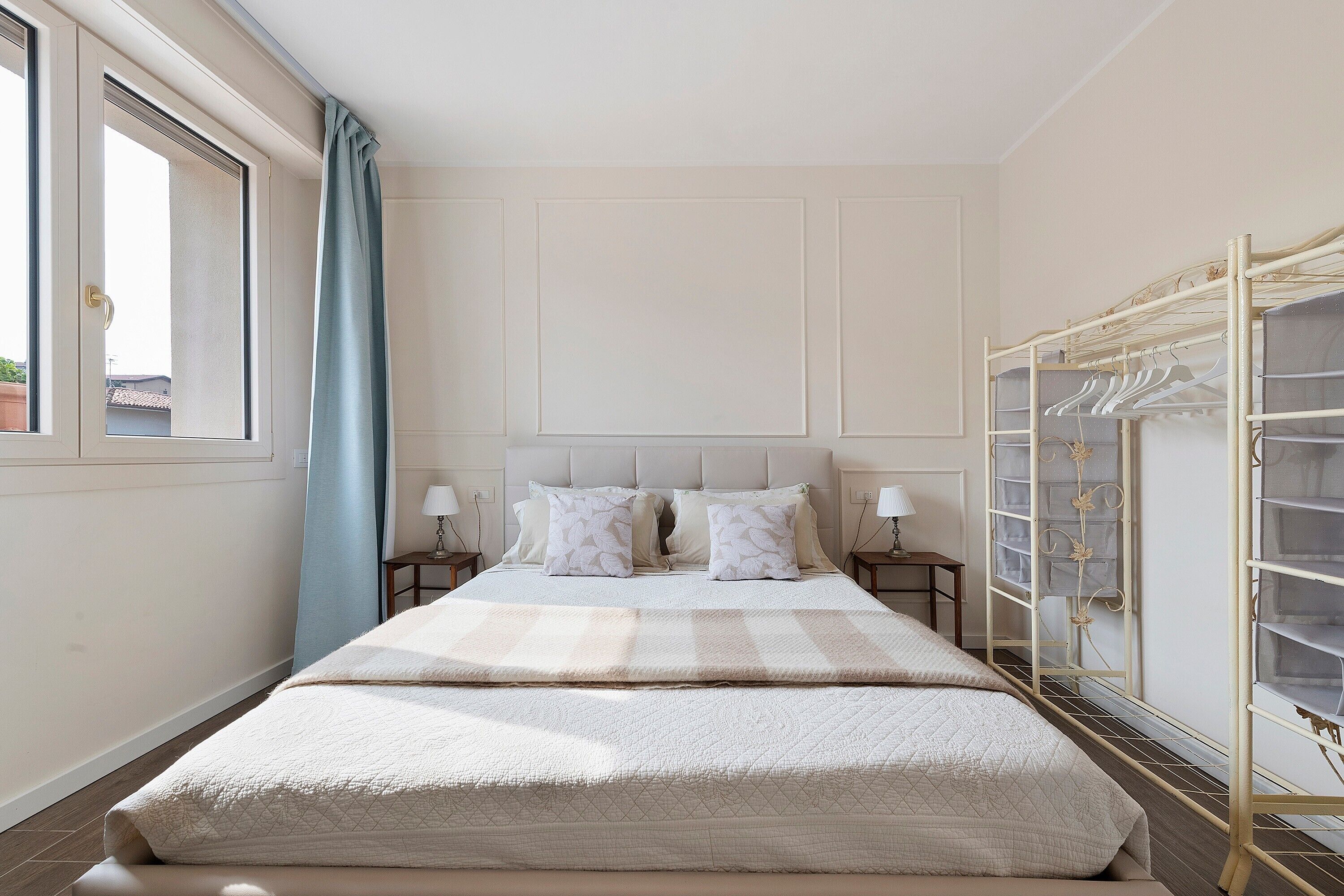 Une chambre à coucher comprenant un lit, des tables de chevet, une fenêtre avec des rideaux et une armoire avec un espace pour suspendre les vêtements.