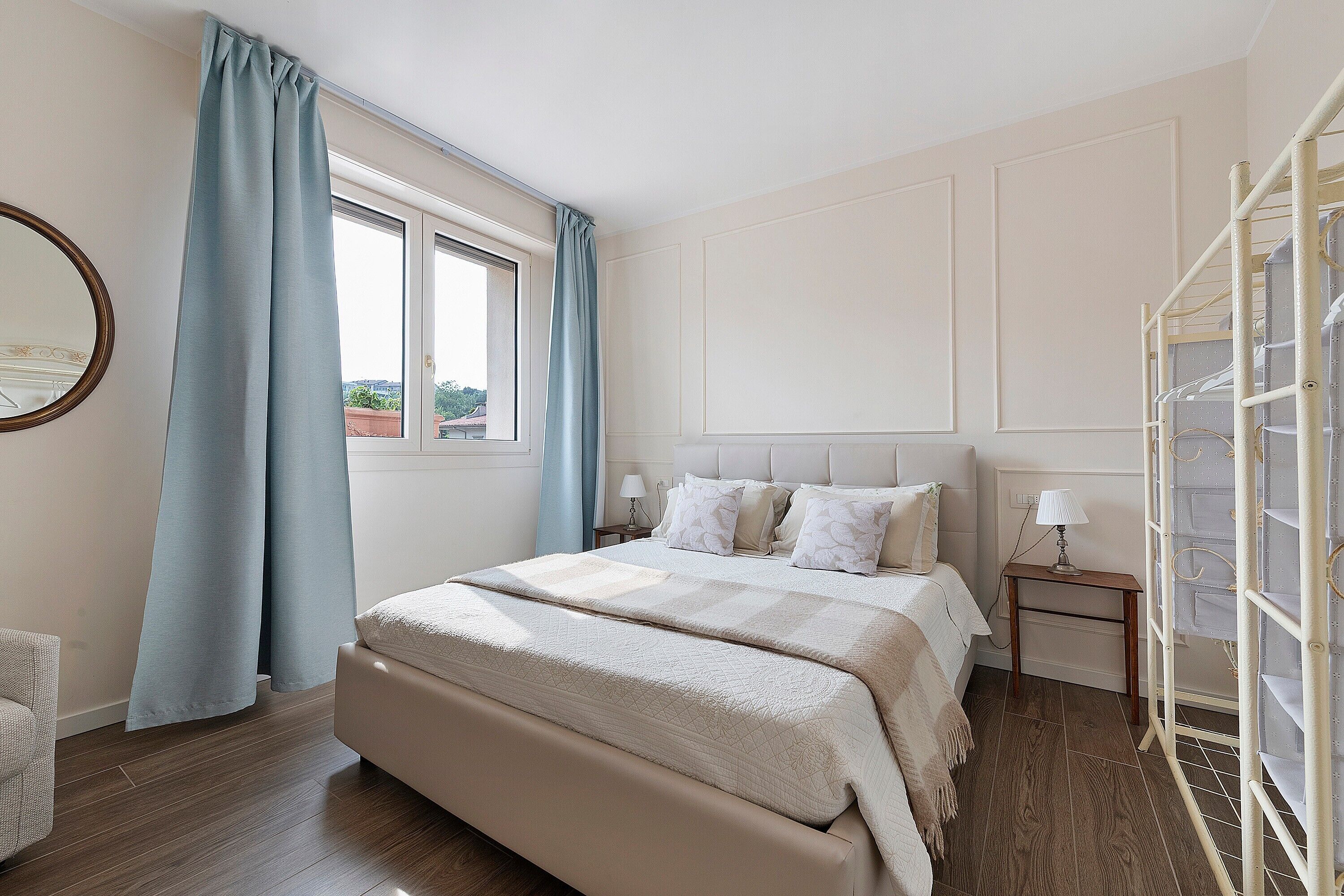 A bedroom with a bed, a window with curtains, a bedside table with a lamp, and a wardrobe with a ladder.