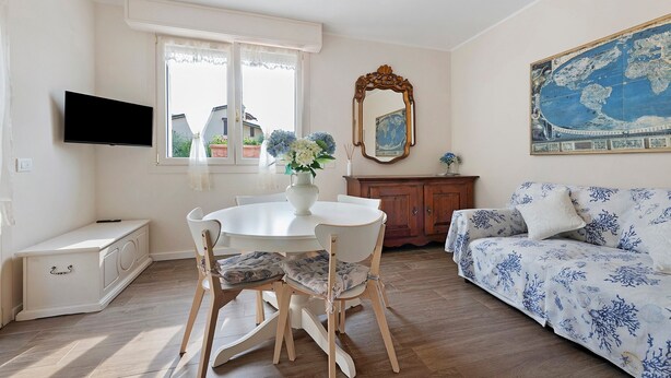 A room with a dining table, chairs, a sofa, a television, a window with curtains, a mirror, and a world map on the wall. - ‘Elegant Lake Iseo’ Apartment with Lake & Mountain Views, Wi-Fi, Air Conditioning (Paratico)