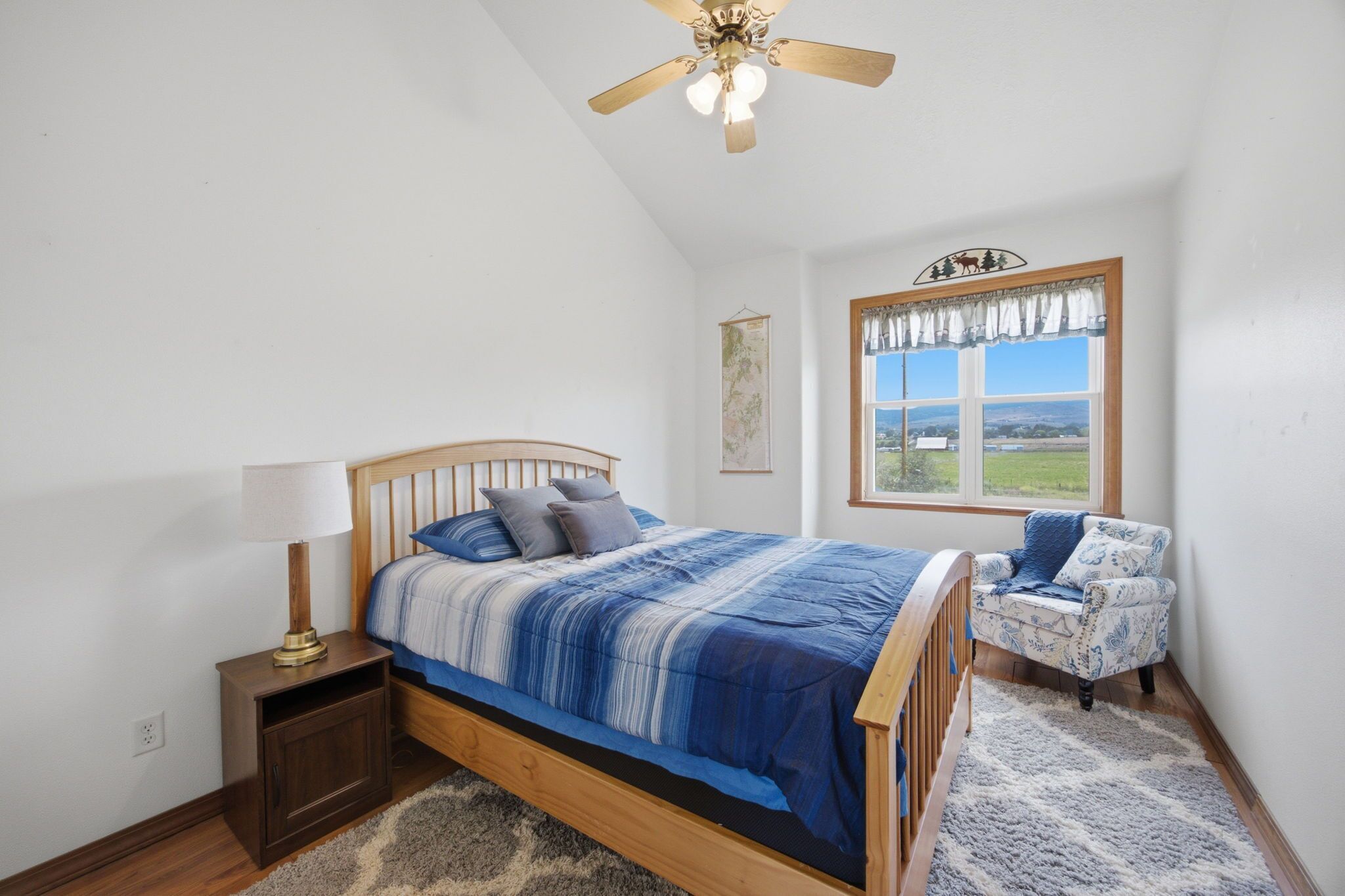A bedroom with a bed, a nightstand, a chair, a window with a view, and a ceiling fan.