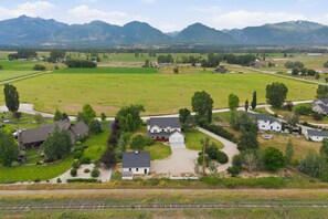A rural residential area with houses, a large green field with hay bales, and mountains in the background. - This Charming farmhous style home is situated just outside Corvallis Montana. The space is well appointed and with plenty of space to spread out, making it a great base for exploring the Bitterroot Valley with family and friends. (Corvallis)