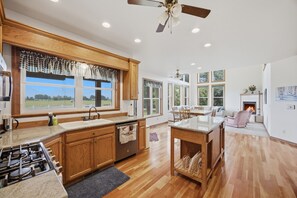 A spacious kitchen with wooden cabinets, a gas stove, and a large window overlooking a green landscape. - This Charming farmhous style home is situated just outside Corvallis Montana. The space is well appointed and with plenty of space to spread out, making it a great base for exploring the Bitterroot Valley with family and friends. (Corvallis)