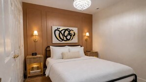 A bedroom with a bed, bedside lamps, a wall-mounted artwork, and a chandelier. - Chef's Château Suite B | Queen Bed, Pool + Hot Tub (Spalding County)