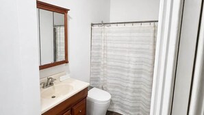 A bathroom with a white sink, wooden vanity, a toilet, and a shower curtain. - Chef's Château Suite B | Queen Bed, Pool + Hot Tub (Spalding County)
