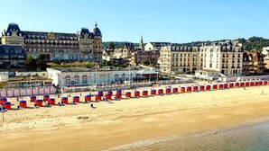 A beach with rows of beach umbrellas and sun loungers, a large building with a dome, and a church with a tall spire. - Houlgate, near the beach, with outdoor space and parking (Houlgate)