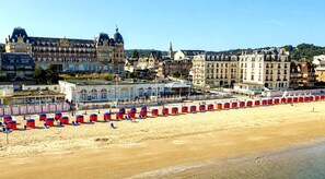 Ein Strand mit Reihen von Strandstühlen und Sonnenschirmen, ein großes Gebäude mit einer Kuppel und eine Kirche mit einem hohen Turm.