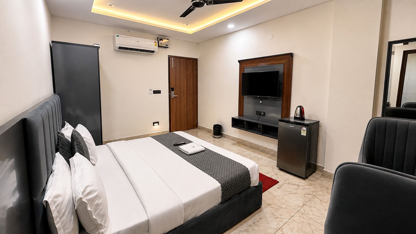 Habitación de hotel con cama, televisión, minibar y ventilador de techo.