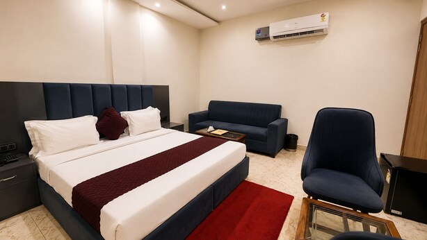 A hotel room with a bed, a sofa, a chair, a nightstand, and an air conditioning unit. - Hotel The Stay (Zirakpur)