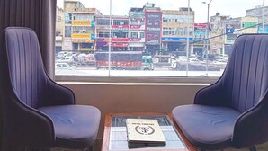A room with two chairs facing a large window overlooking a cityscape with various buildings and a busy street. - Hotel The Stay (Zirakpur)