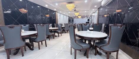 Interior de restaurante con paredes de mármol, mesas redondas y sillas.