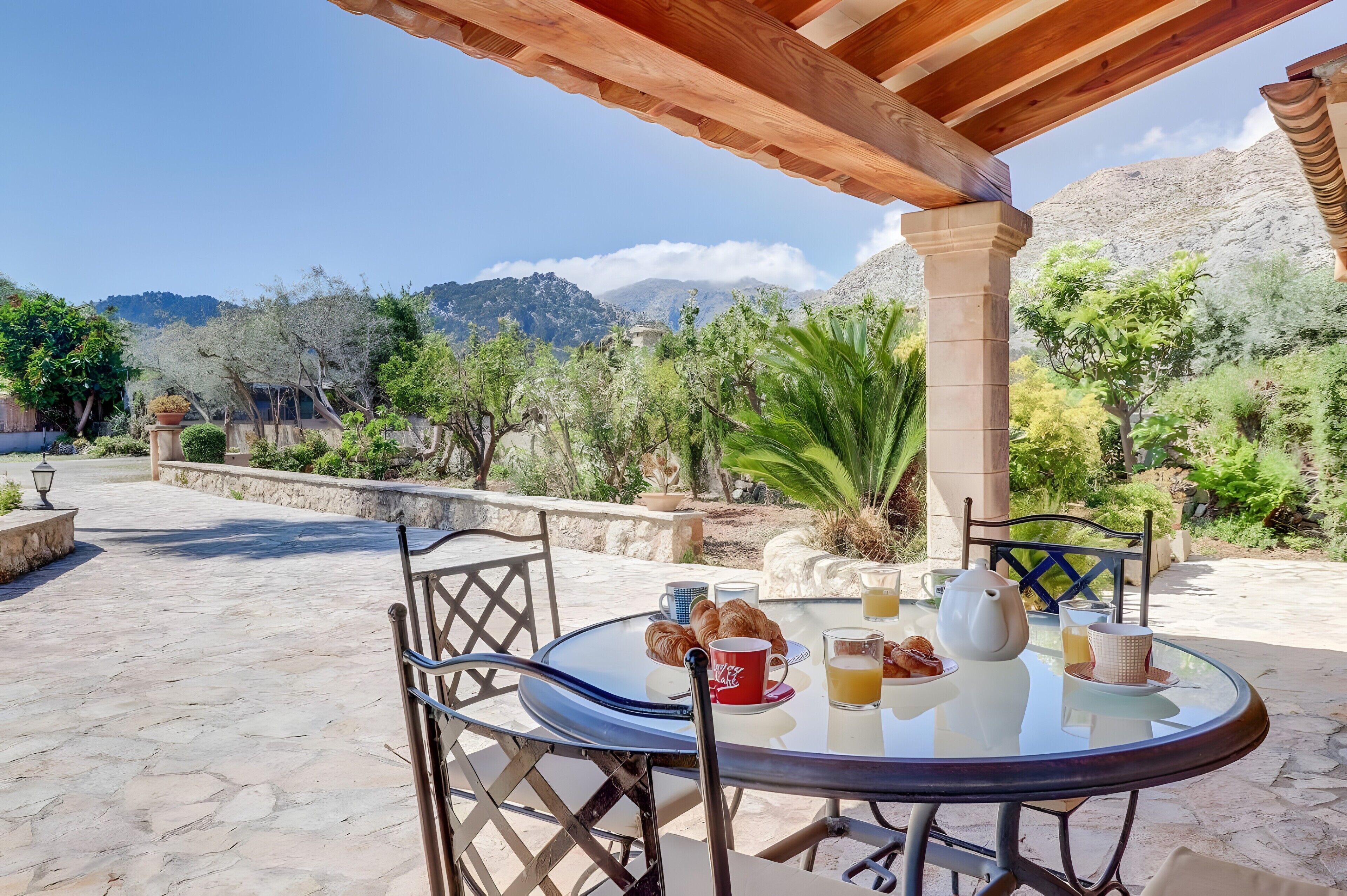 Mesa redonda de vidrio con sillas, una escena de desayuno y un paisaje montañoso de fondo.