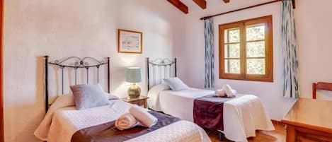 A room with two beds, a window with curtains, a lamp, and a painting on the wall.