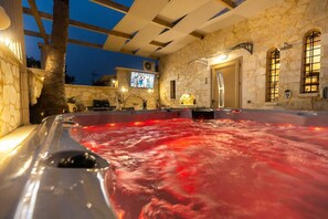 Un bain à remous avec un mur en pierre en arrière-plan, un téléviseur fixé au mur et une porte donnant sur une autre pièce.