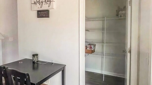 Uma área de refeições com uma mesa e cadeiras, uma parede com uma frase emoldurada e vista para um espaço com uma estante.