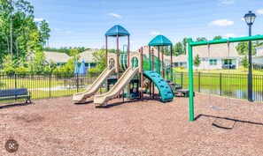 Ein Spielplatz mit Rutschen und Schaukeln, umzäunt und von Bäumen gesäumt.