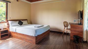 Een slaapkamer met een houten bed, een bureau met stoel, een televisie en een raam met uitzicht.