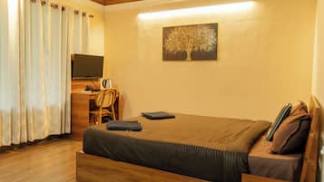 Un dormitorio con cama, escritorio y silla, televisor y un cuadro de un árbol en la pared.