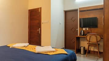 Una habitación de hotel con cama, escritorio, silla, televisor y basurero.