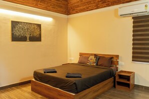 A bedroom with a wooden bed, a nightstand, a wall-mounted air conditioner, and a painting of a tree. - Bruce and Bells Nature resort  (Kothamangalam)