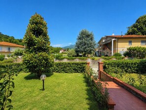 A well-maintained garden with a lawn, a tall tree, and a pathway leading to a building with a tiled roof. - Casa Ivo | Relaxation between Lucca and Collodi (Capannori)